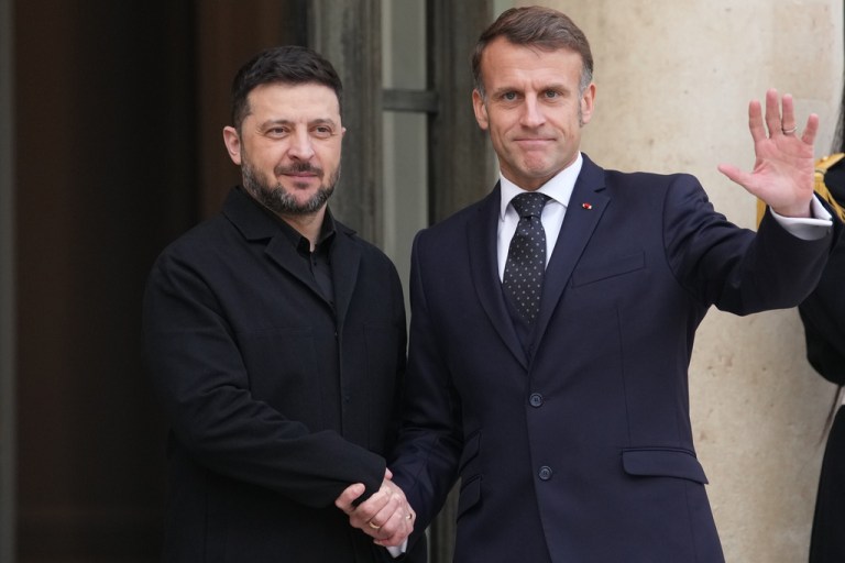 French President Emmanuel Macron waves as he shakes hands with Ukrainian President Volodymyr Zelensky.