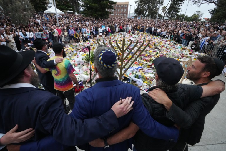 Mourners gather at a menorah lighting ceremony at a floral memorial for victims of the Bondi Beach shooting.