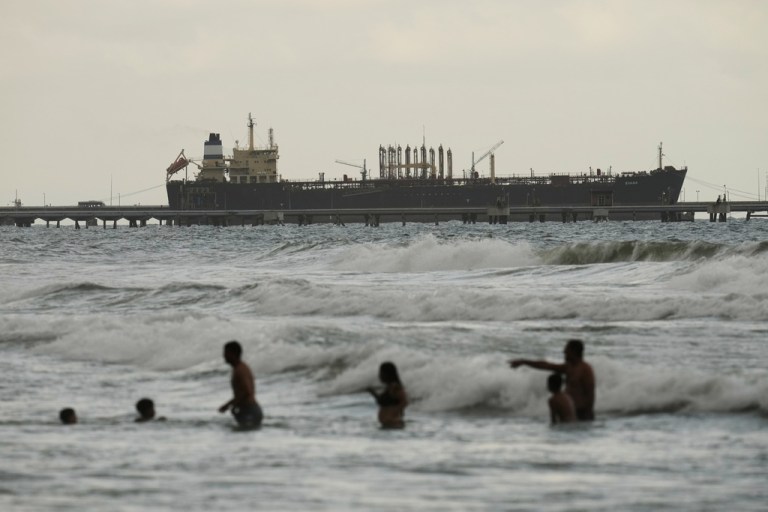 People play in the ocean with an oil tanker in the background.