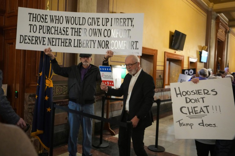Protesters hold signs outside the Indiana Senate chamber before a vote to redistrict the state's congressional map.