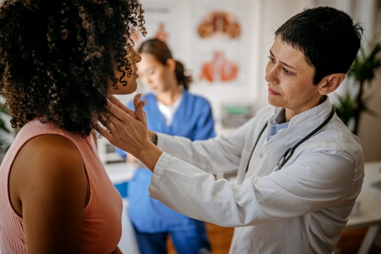 Female doctor examining a female patient in his medical office while female nurse writing information about patient