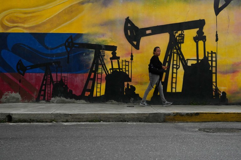 A local walks past a mural featuring oil pumps and wells in Caracas, Venezuela.