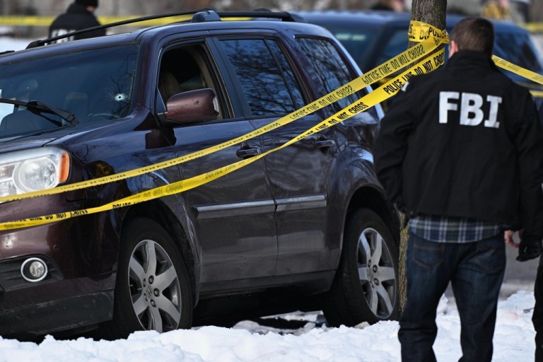 A bullet hole is seen in the windshield as law enforcement officers work the scene of a shooting involving federal law enforcement agents.
