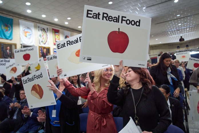 Staff and attendees of an announcement by Health and Human Services Secretary Robert F. Kennedy Jr., applause while holding drawings of foods, at Health and Human Services Headquarters, Thursday, Jan. 8, 2026, in Washington. (AP Photo/Jacquelyn Martin)