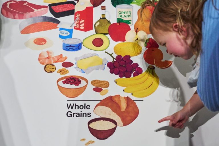 Elle, 18 months, reaches toward the bread at the bottom of the revised food pyramid while held by her mother Claire Dooley, after an announcement by Health and Human Services Secretary Robert F. Kennedy Jr., regarding nutrition policy, at Health and Human Services Headquarters, Thursday, Jan. 8, 2026, in Washington. (AP Photo/Jacquelyn Martin)