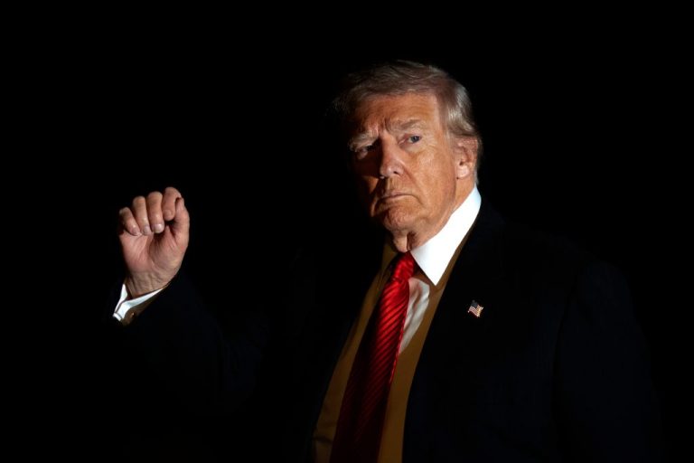President Donald Trump is illuminated by a camera flash as he gestures while walking across the South Lawn of the White House.