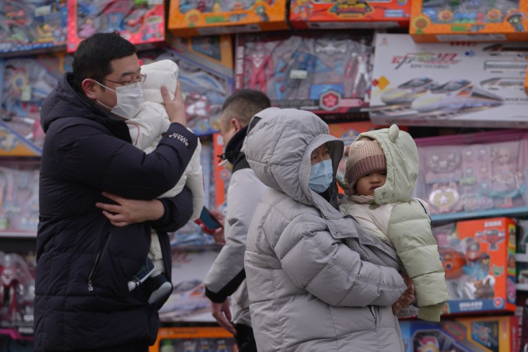 People carry their toddlers by a toy store in Beijing, Monday, Jan. 19, 2026.