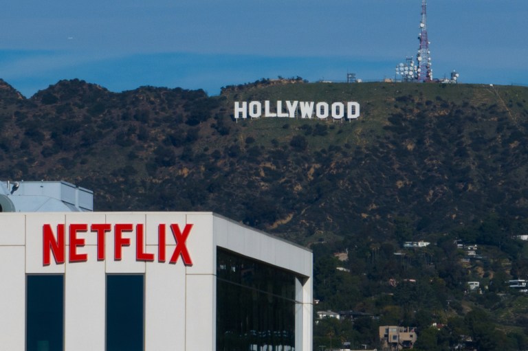 A Netflix sign atop a building in Los Angeles, with the Hollywood sign in the distance.