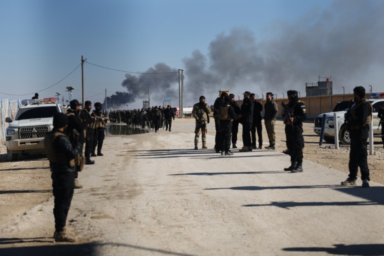 Syrian government forces patrol inside the al Hol camp as smoke rises from an arms depot explosion.