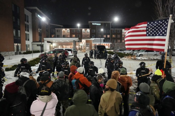 Demonstrators stand against law enforcement officers during a protest outside SpringHill Suites and Residence Inn by Marriott hotels on Monday, Jan. 26, 2026, in Maple Grove, Minn. (AP Photo/Adam Gray)
