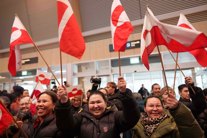 People wave by national flags while listening a speech of Greenland Minister for Foreign Affairs and Research Vivian Motzfeldt after her arrival at airport of Nuuk, Greenland, on Tuesday, Jan. 20, 2026. (AP Photo/Evgeniy Maloletka)