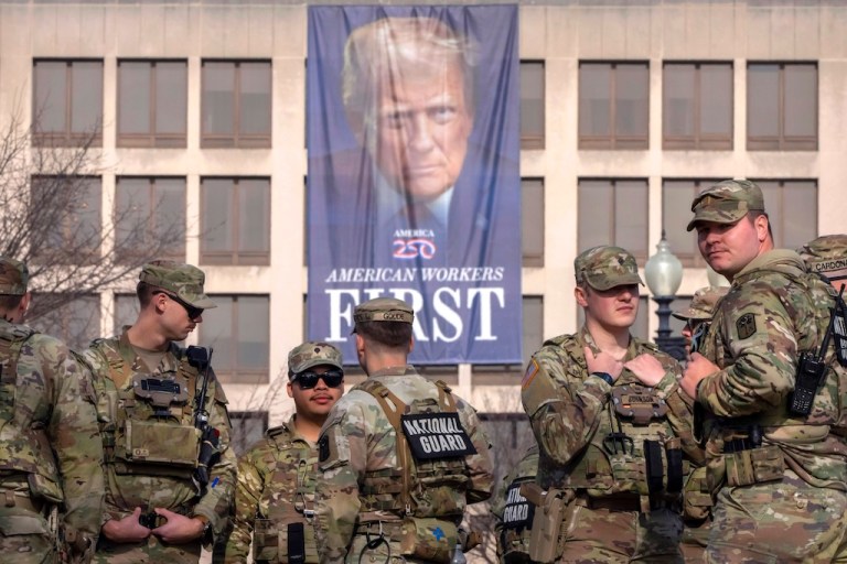 National Guard members gather near a large portrait of President Donald Trump on the Labor Department headquarters before the body of Metropolitan Police Department officer Terry Bennett is driven past the Capitol on Jan. 8, 2026, in Washington. (AP Photo/Mark Schiefelbein)