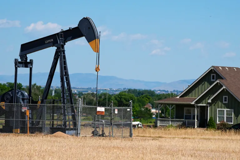 A pumpjack works on a pad near a housing development.