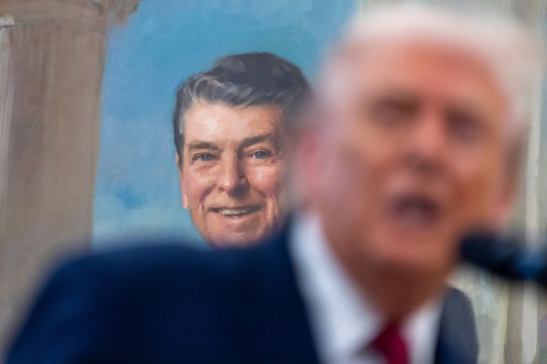 Former President Ronald Reagan smiles in a portrait over the shoulder as President Donald Trump speaks