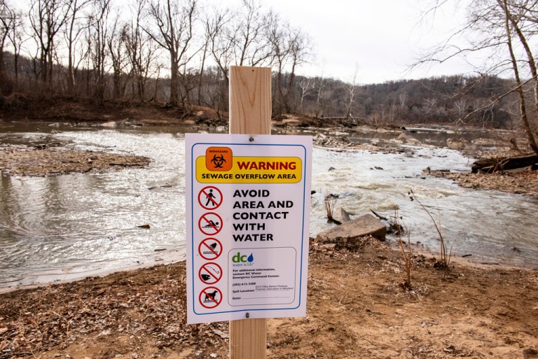 A recently placed warning sign is seen at the sight of a massive pipe rupture, as sewage flows into the Potomac River, right, in Glen Echo, Md., Friday, Jan. 23, 2026. A massive pipe that moves millions of gallons of sewage has ruptured and sent wastewater flowing into the Potomac River northwest of Washington, polluting it ahead of a major winter storm that has repair crews scrambling. (AP Photo/Cliff Owen)