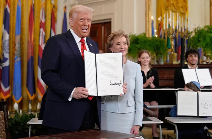 President Donald Trump holds up a signed executive order abolishing the Education Department, alongside Secretary of Education Linda McMahon, in the White House on March 20, 2025. Children are seated nearby, signing their own versions of the executive order. (Ben Curtis/AP)