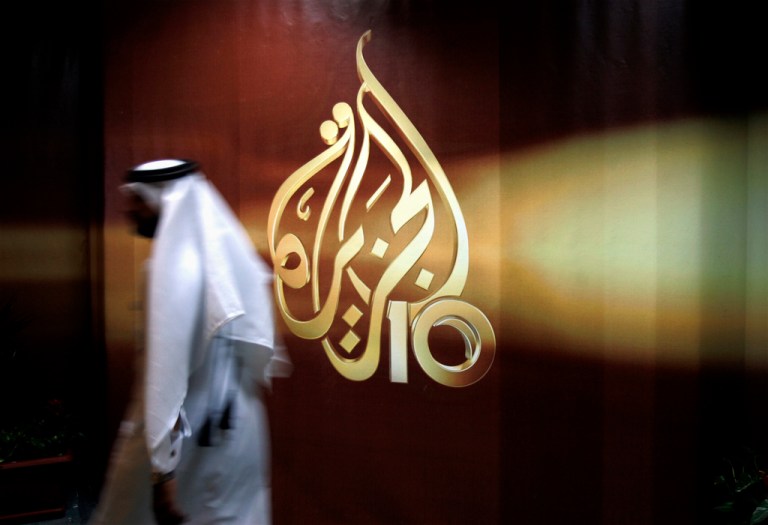 A Qatari employee walks past a logo of Al Jazeera in Doha