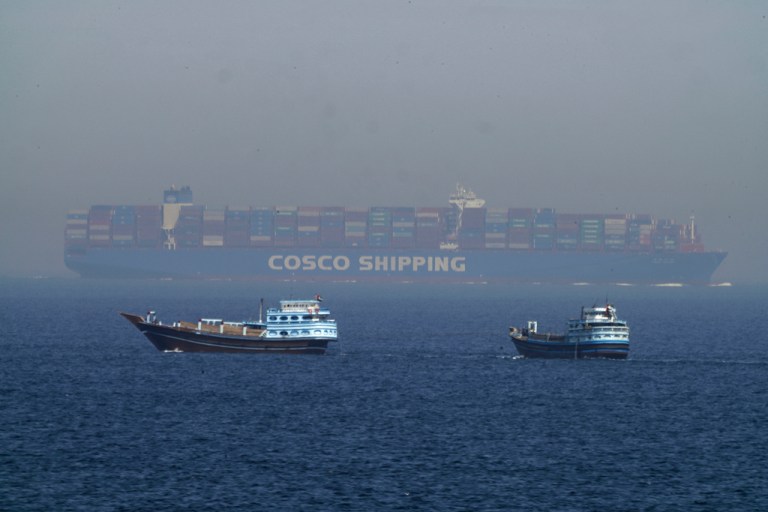 Two traditional dhows sail by a large container ship in the Strait of Hormuz.