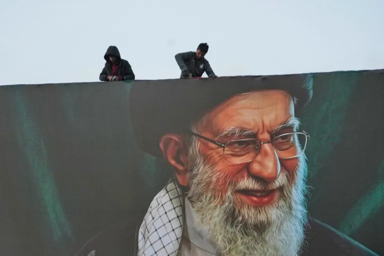 Workers install a billboard on an overpass containing a portrait of the late Iranian Supreme Leader Ayatollah Ali Khamenei.