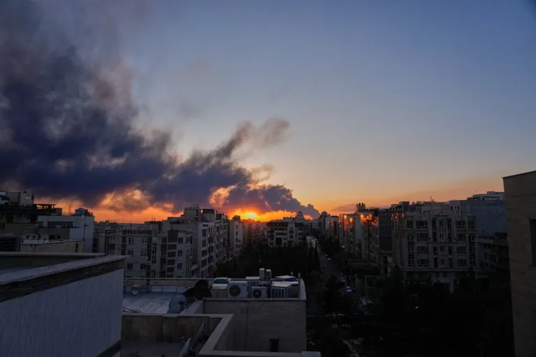 The sun sets behind a plume of smoke rising after a U.S.-Israeli military strike in Tehran, Iran.