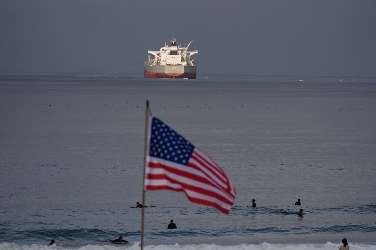 Surfers wait for waves on El Porto Beach as the crude oil tanker 