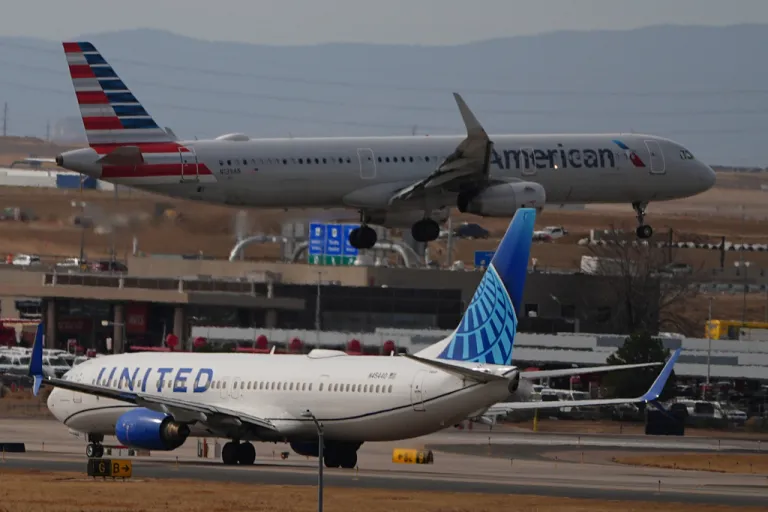 An American Airlines jetliner lands on a runway as a United Airlines plane waits for clearance to take off as high winds strafe Denver International Airport Thursday, March 12, 2026, in Denver. (AP Photo/David Zalubowski)