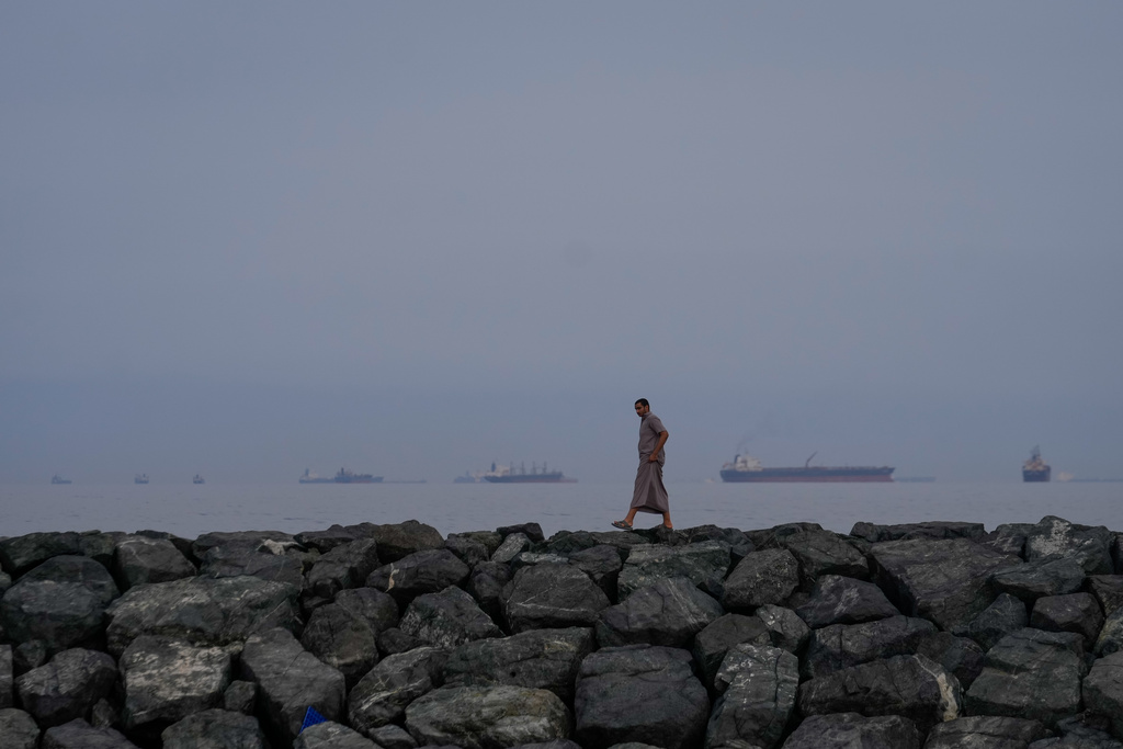 FILE - A man walks along the shore as oil tankers and cargo ships line up in the Strait of Hormuz, as seen from Khor Fakkan, United Arab Emirates, Wednesday, March 11, 2026. 