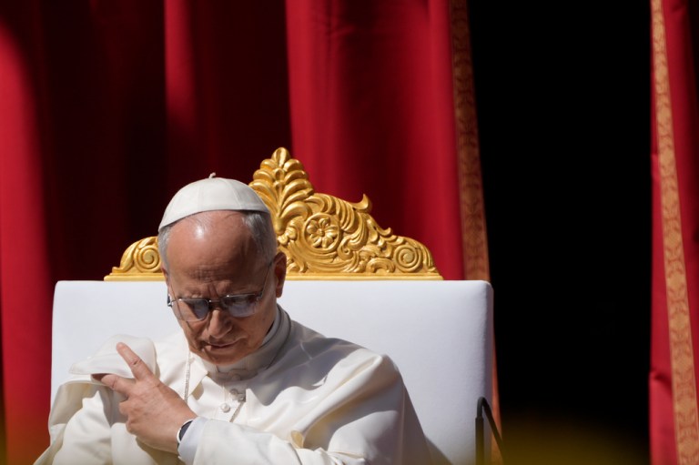 Pope Leo XIV sits on a throne in front of a red curtain