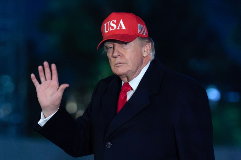 Trump waves while wearing a red USA hat