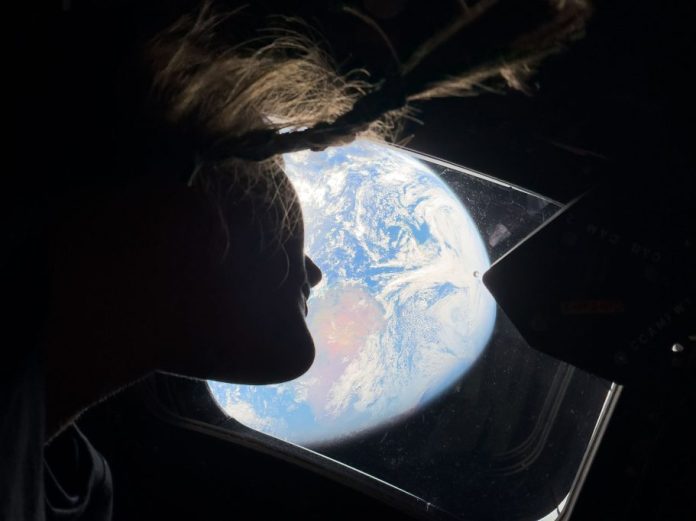 NASA astronaut and Artemis II mission specialist Christina Koch peers out of one of the Orion spacecraft's main cabin windows, looking back at Earth.