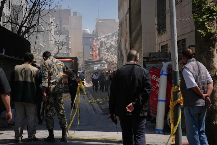 Bystanders watch from a distance as rescue teams and first responders work at the site of a strike that, according to a security official at the scene, destroyed half of the Khorasaniha Synagogue and nearby residential buildings in Tehran, Iran, Tuesday, April 7, 2026. (AP Photo/Francisco Seco)