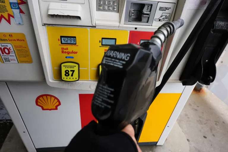 A gas price is displayed as a customer holds a fuel pump nozzle before filling up her vehicle's gas tank at a gas station.
