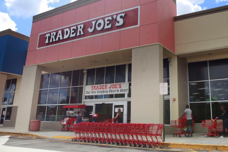 People stand in line waiting to enter Trader Joe's to buy groceries.